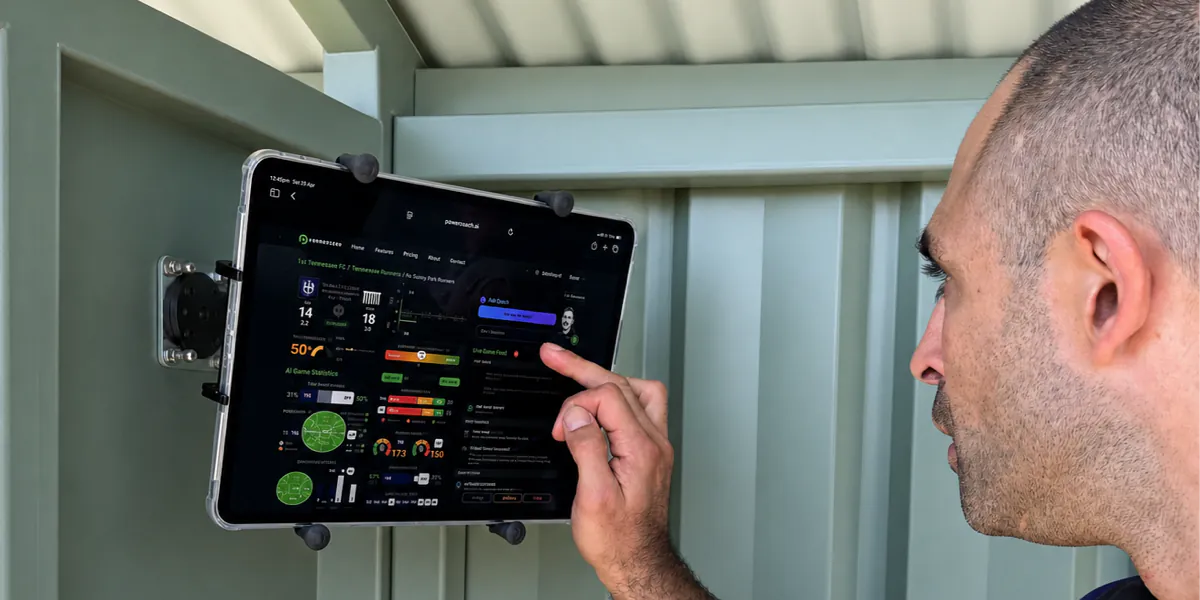 Coach reviewing the Powercoach dashboard on a wall-mounted iPad in the coaches' box